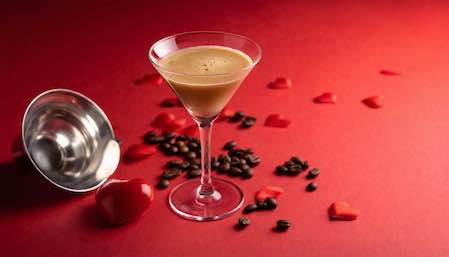 An espresso martini surrounding by hearts and coffee beans
