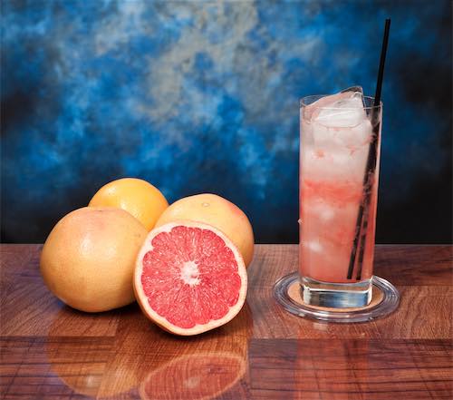 A tall glass of greyhound cocktail, with some grapefruits